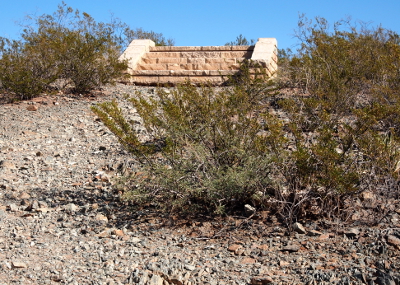 [A long expanse of sagebrush and dirt backed by a row of continuous rock mounds all below a very blue sky.]